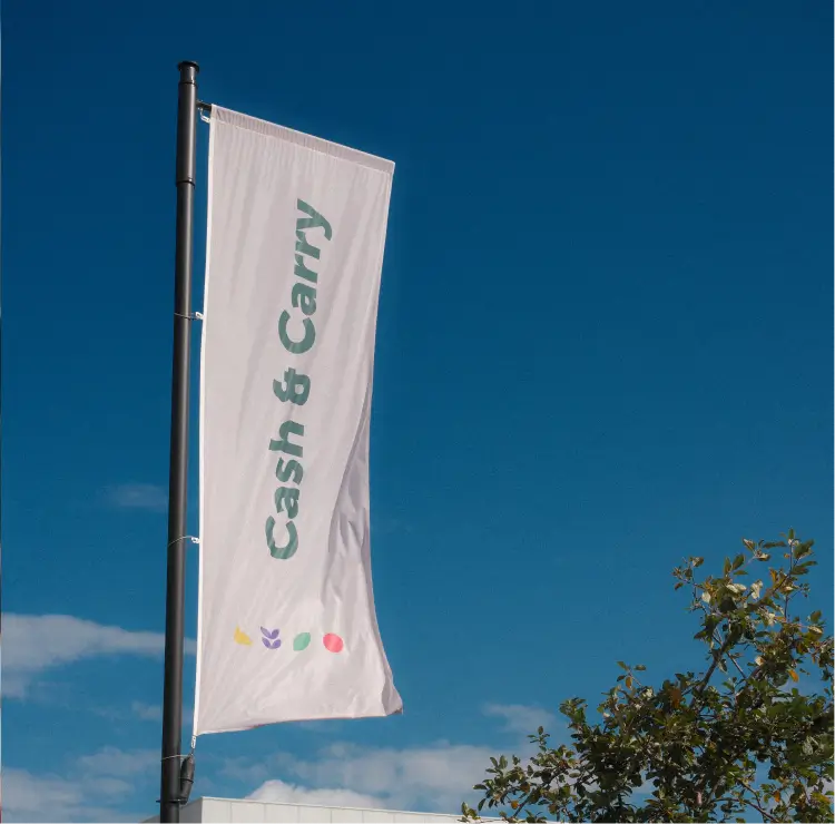 Vlag met tekst 'Cash & Carry' tegen een blauwe lucht met enkele wolken en een boom rechts.