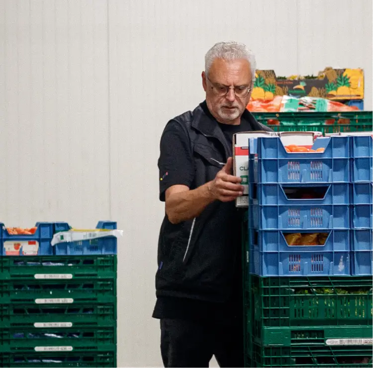 Man pakt een kist met groenten uit stapels blauwe en groene kratten in een magazijn.