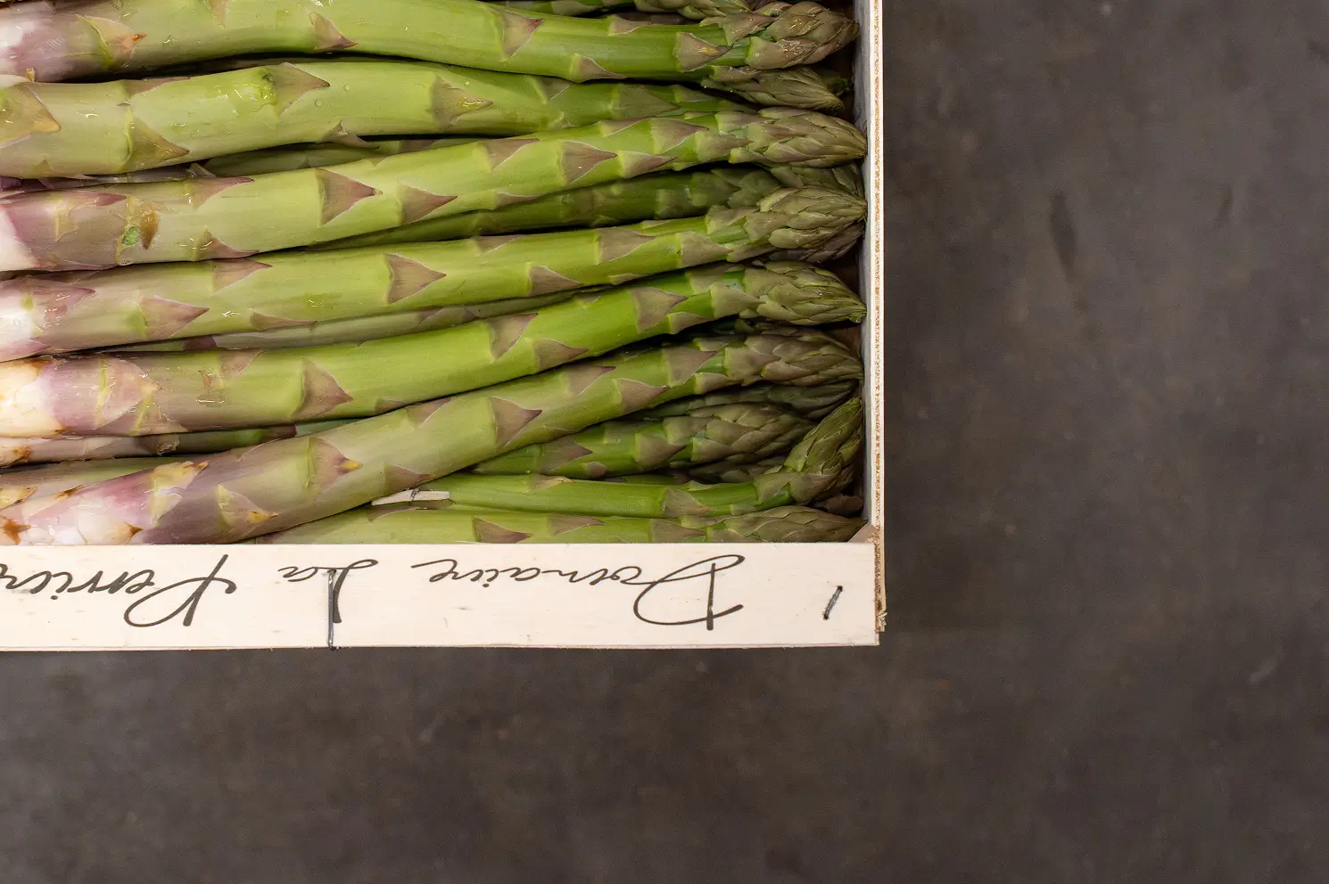 Bos groene asperges netjes gerangschikt in een houten kist op een donkere ondergrond.