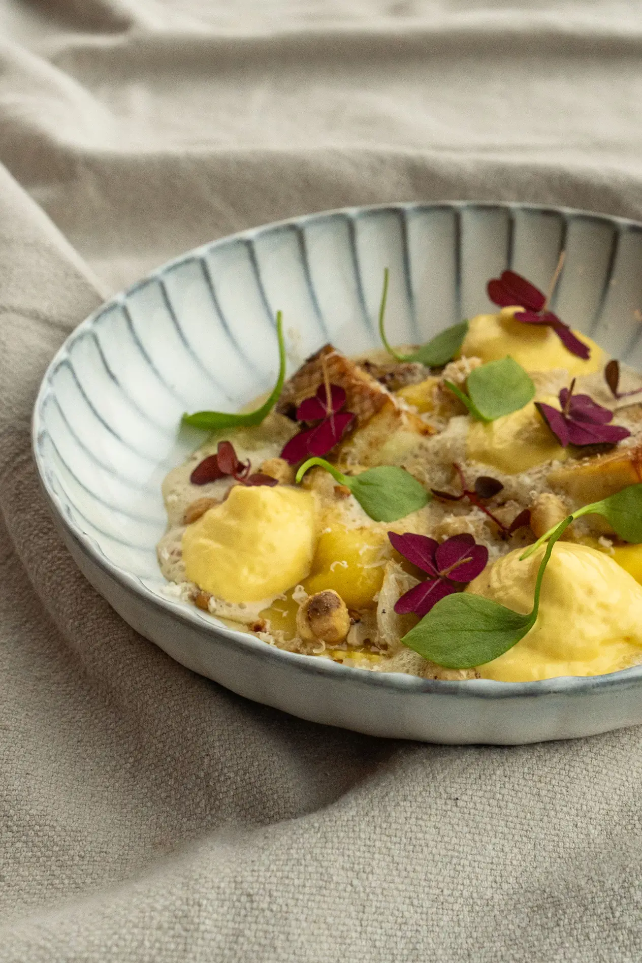 Gerecht met gele mousse, stukjes vis, groene en rode blaadjes in een keramische kom.