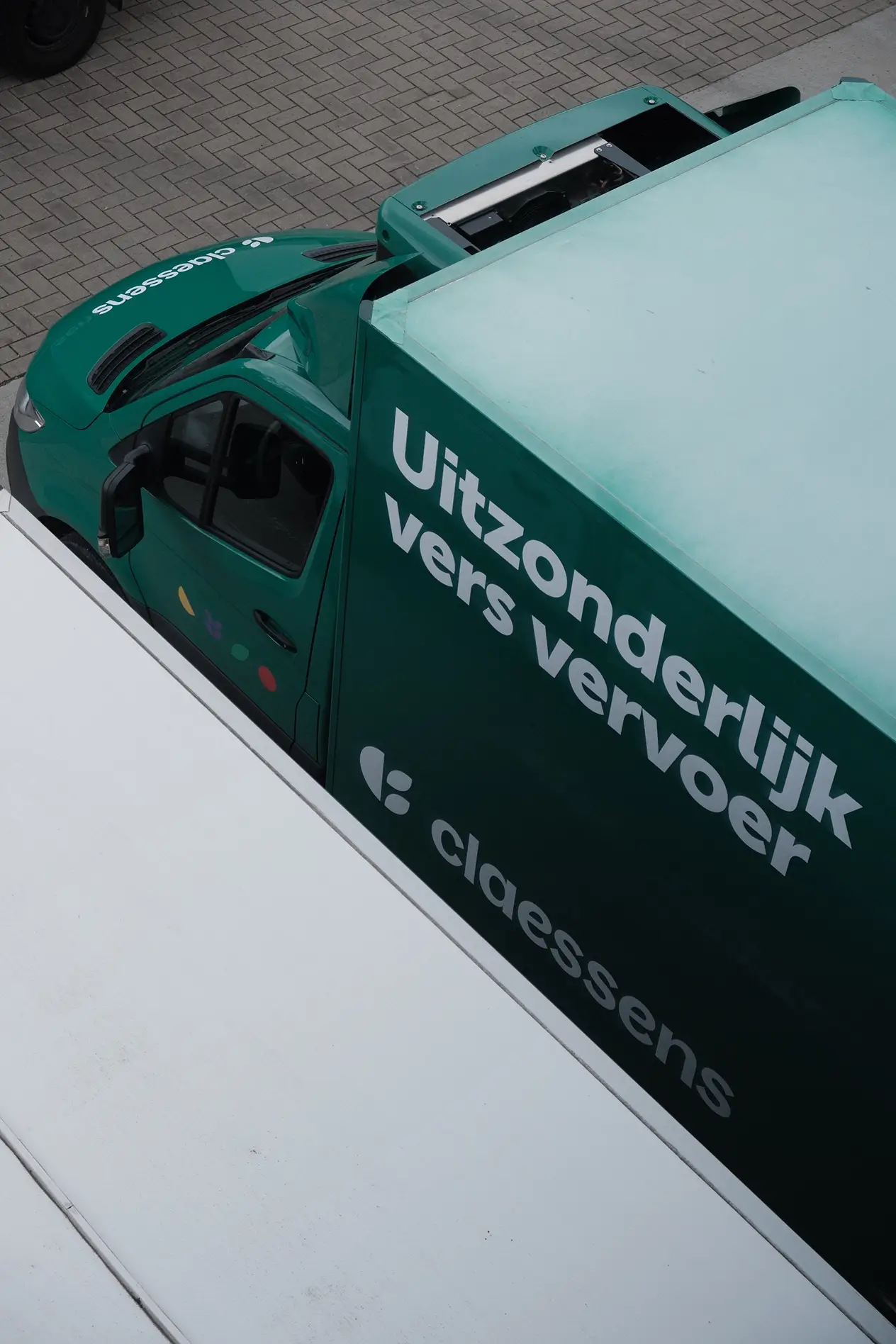 Groene Claessens vrachtwagen met tekst 'Uitzonderlijk vers vervoer' geparkeerd op straat.