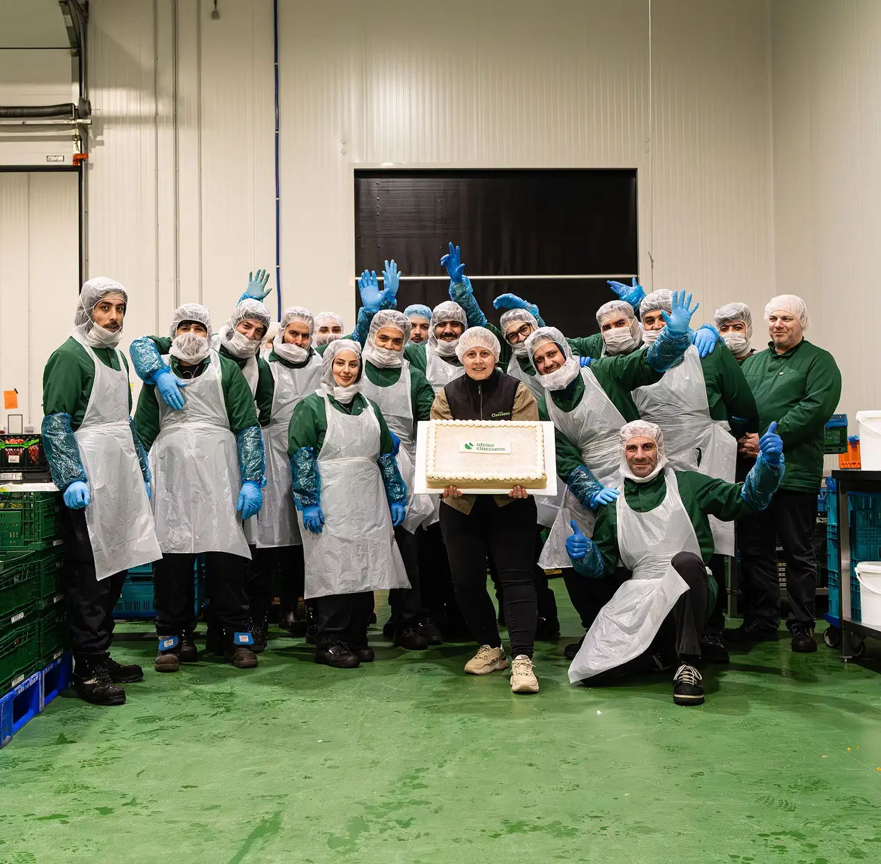 Groep werknemers in beschermende kleding poseert met een taart met het logo van Atelier Clôssens.