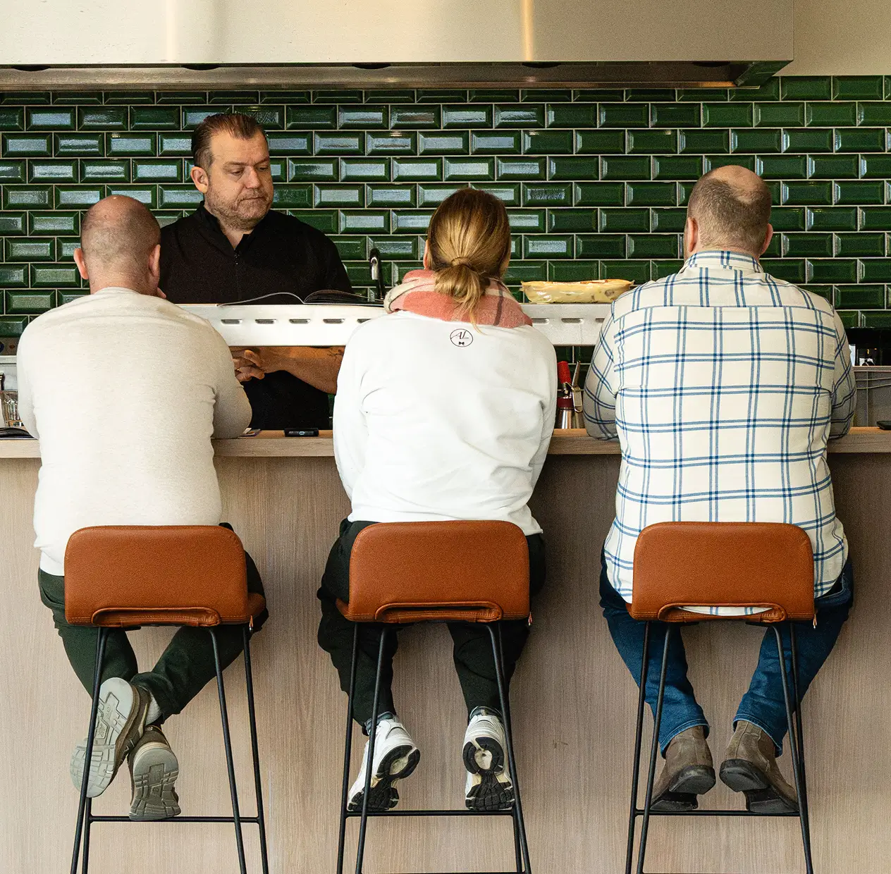Drie mensen zitten op barkrukken aan een bar met een ober aan de achterkant.