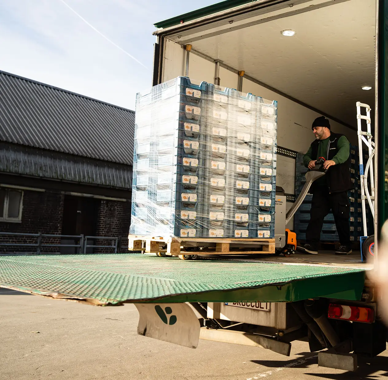 Man bedient een palletwagen met ingepakte kratten op een vrachtwagen laadplatform.