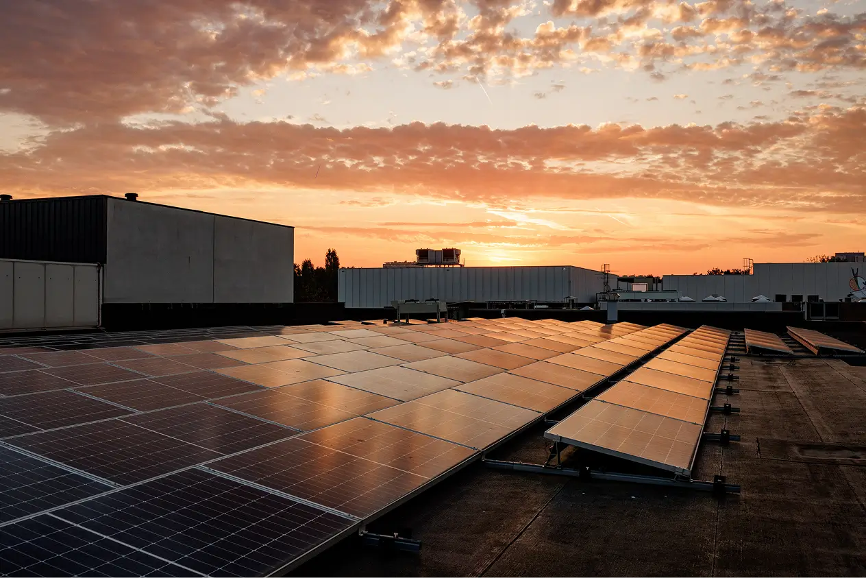 Zonnepanelen op een plat dak bij zonsondergang met oranje en paarse wolken.