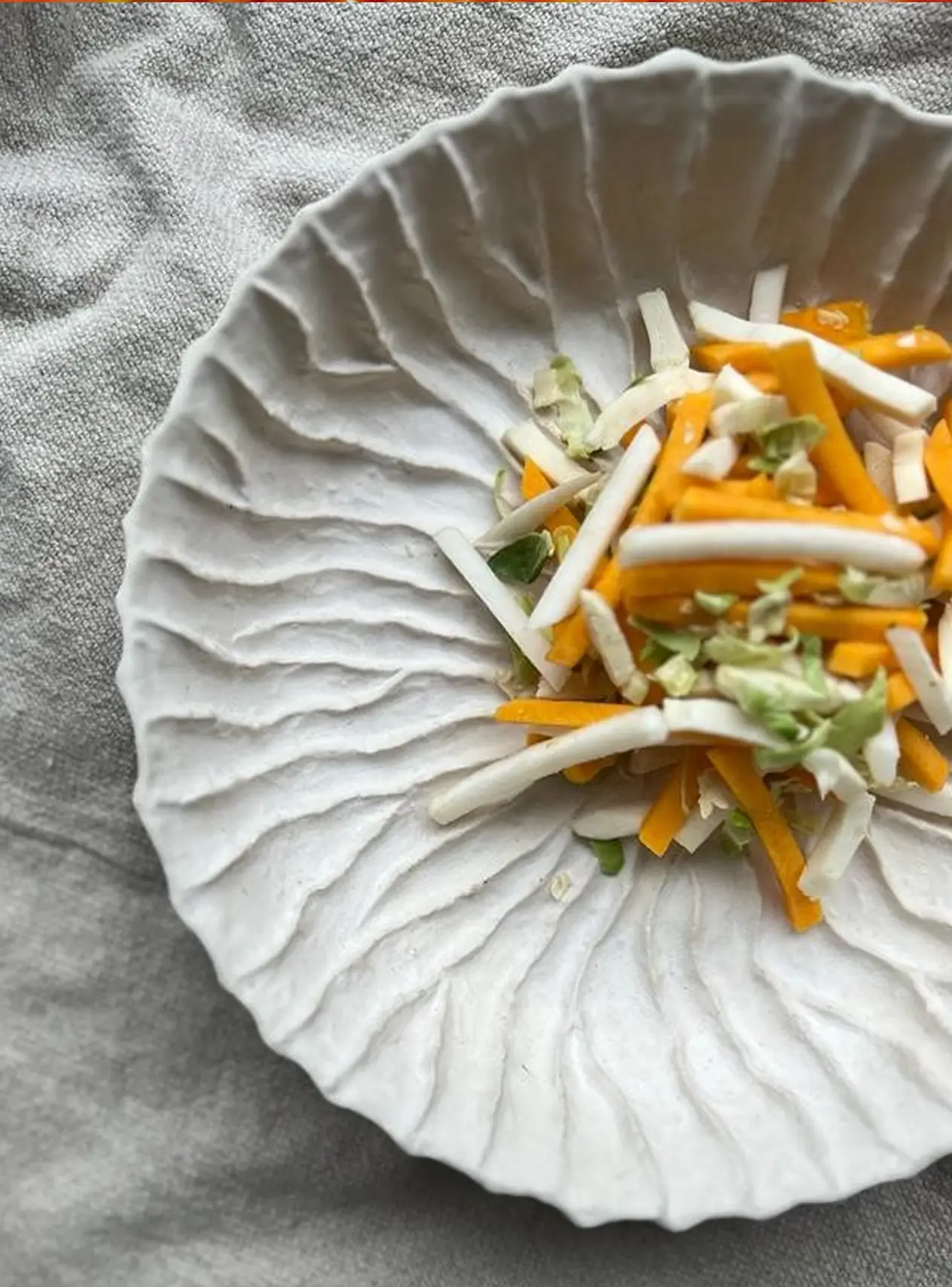 Witte schaal met reepjes witte en oranje groenten op een grijze stofachtergrond.