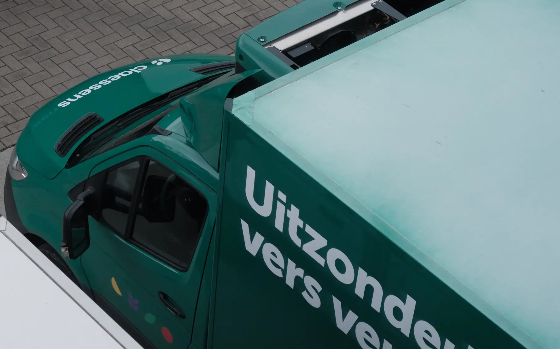 Groene vrachtwagen met tekst 'Uitzonder vers vervoer' geparkeerd op grijze stenen straat.