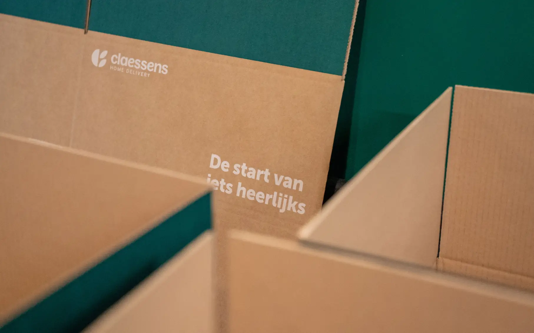 Open kartonnen dozen met tekst ‘De start van iets heerlijks’ en Claessens Home Delivery-logo.