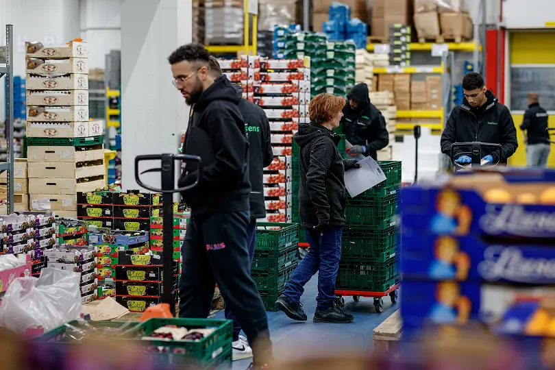 Mensen in een magazijn werken met karren en gestapelde dozen met producten.