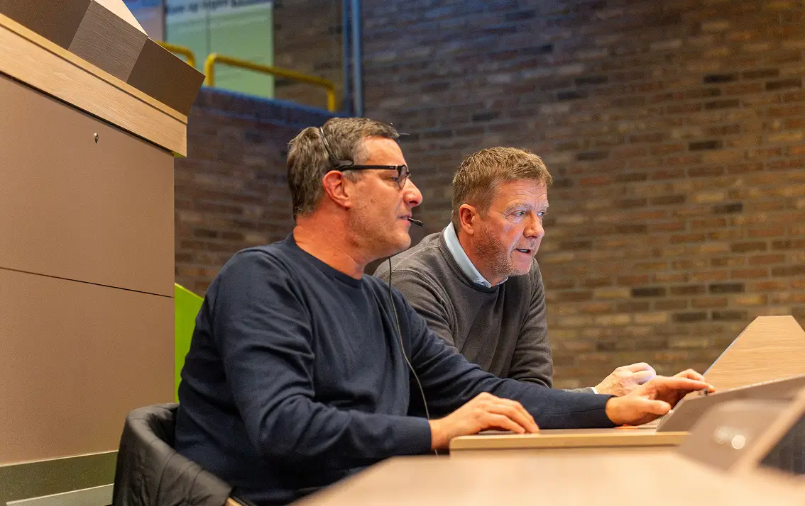 Twee mannen die gefocust naar een computerscherm kijken in een kantooromgeving.
