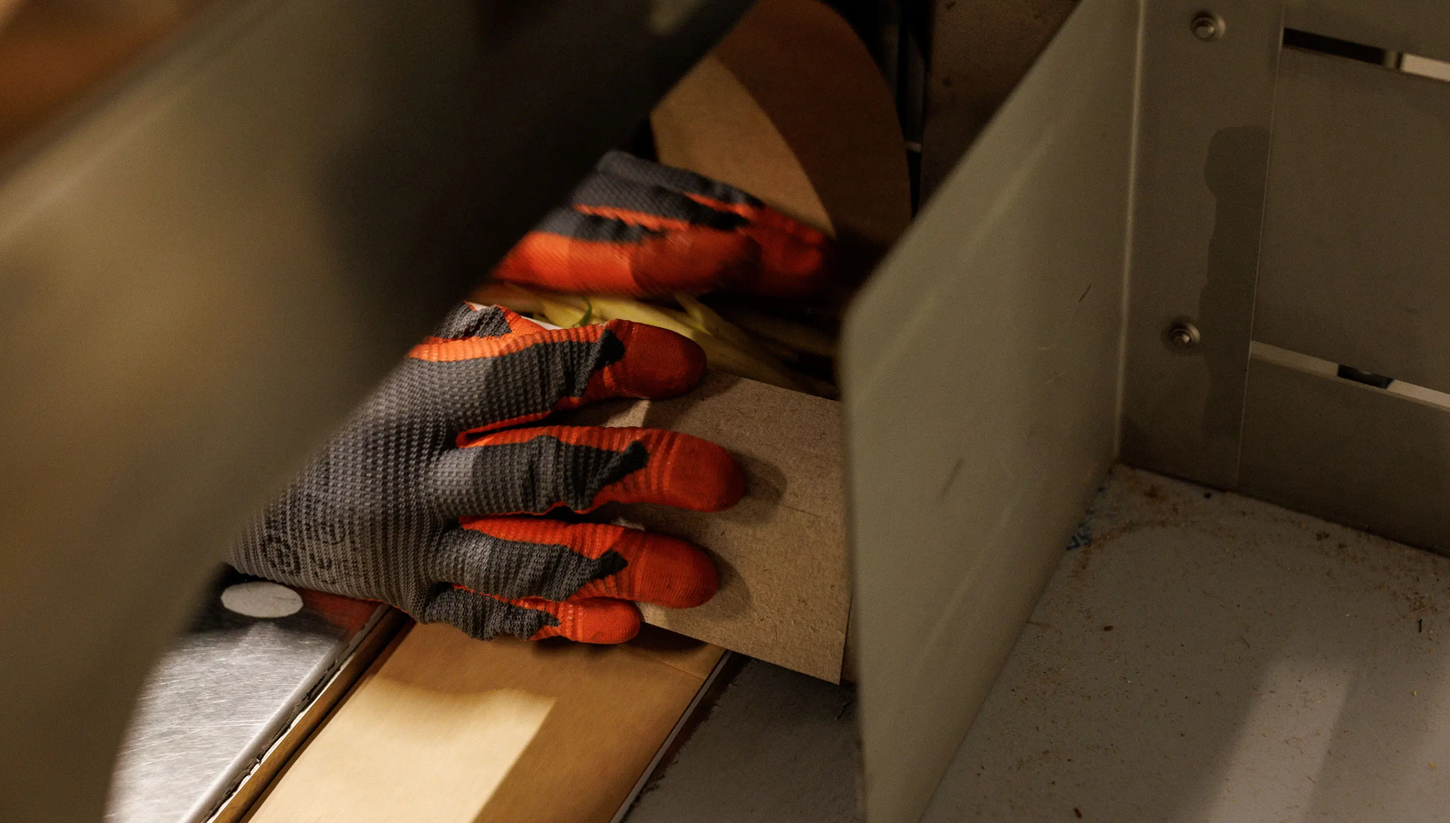 Hand met beschermende handschoen schuift een stuk hout in een machine voor fabricage.