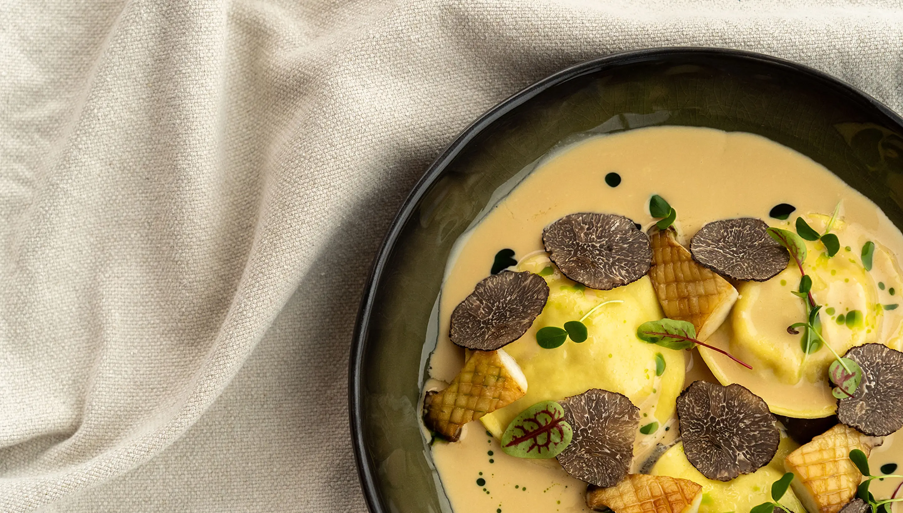 Bord met ravioli in romige saus, gegarneerd met zwarte truffelschijfjes, paddestoelen en groene kruiden.
