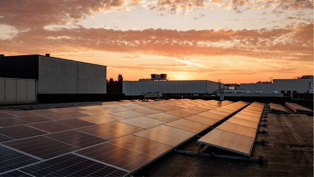 Zonnepanelen op het dak met een zonsondergang en deels bewolkte lucht.