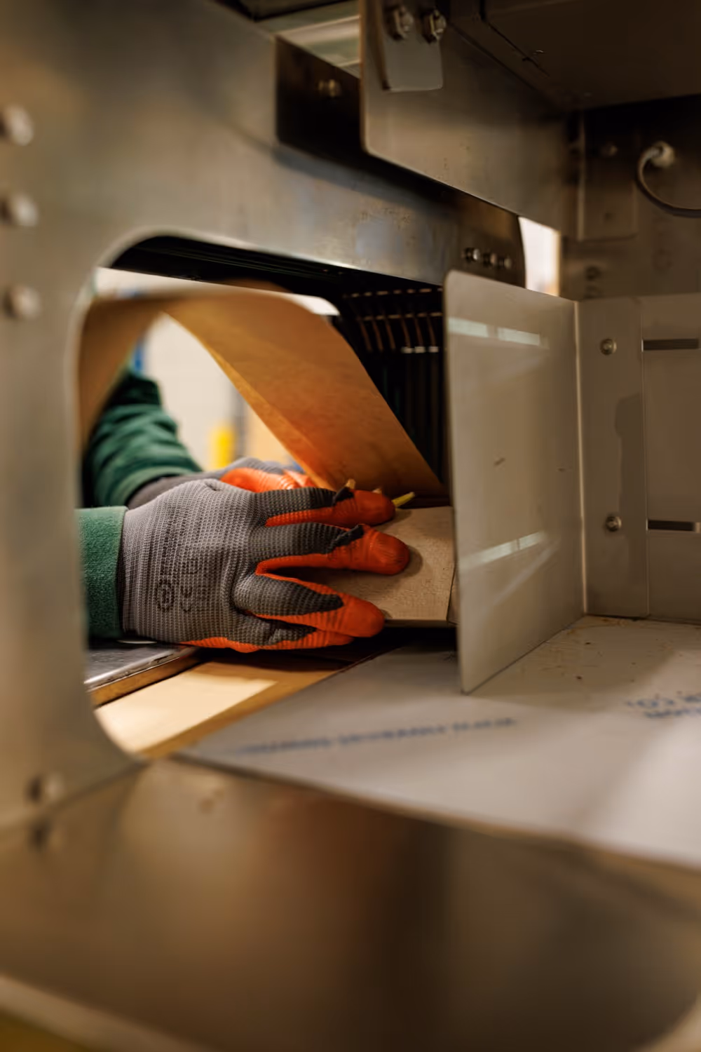 Een persoon met handschoenen plaatst karton in een grote machine voor verwerking.