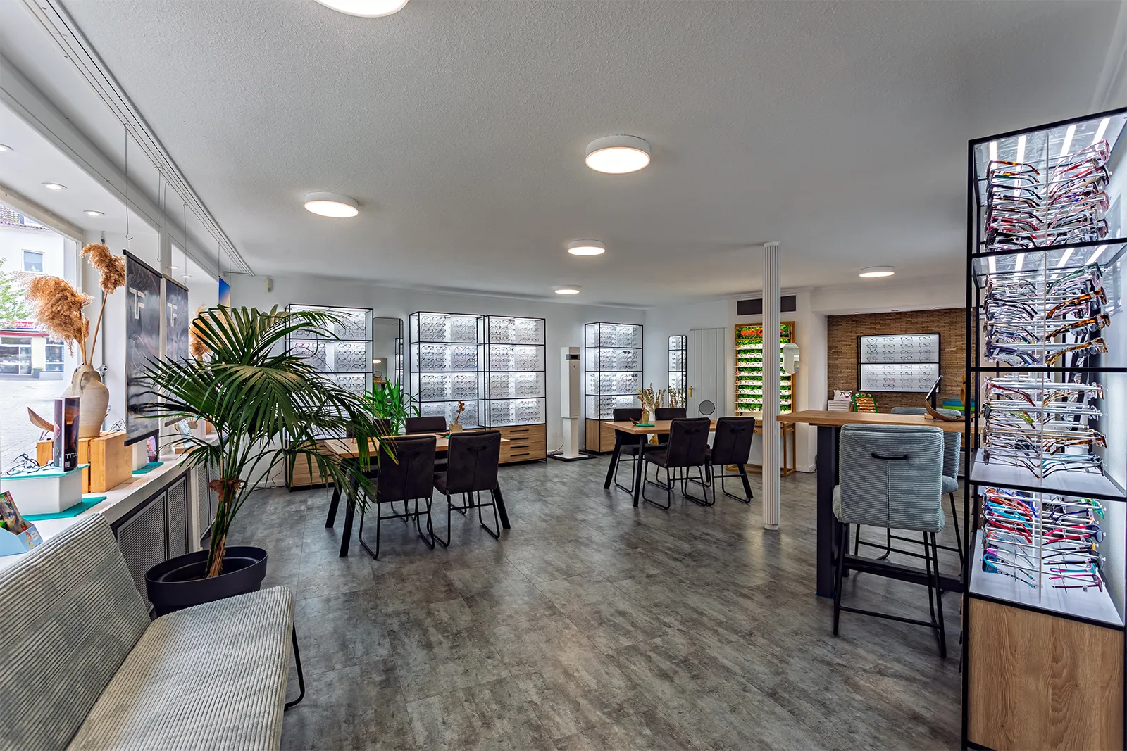 Spacious, modern eyewear store with glasses displayed on shelves and tables with chairs for customers.