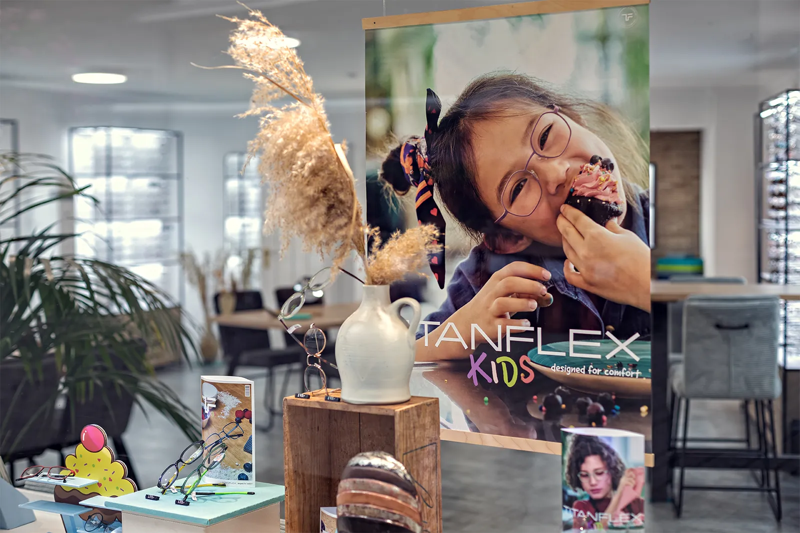 Display of children’s eyeglasses with poster of a child eating a cupcake wearing glasses.