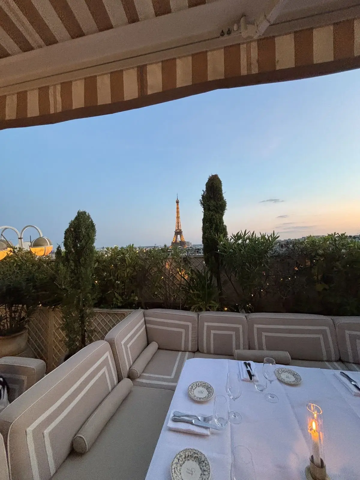 Table dressée sur une terrasse parisienne au crépuscule, canapés crème et vue sur la tour Eiffel.