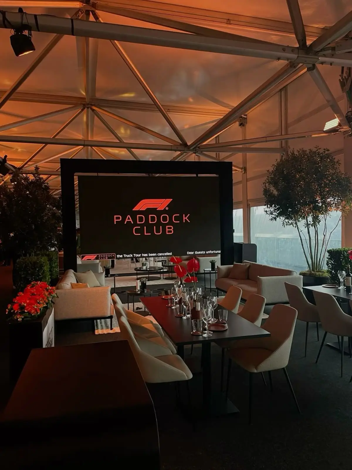 Espace F1 Paddock Club sous une verrière, avec salon, tables dressées et fleurs rouges.