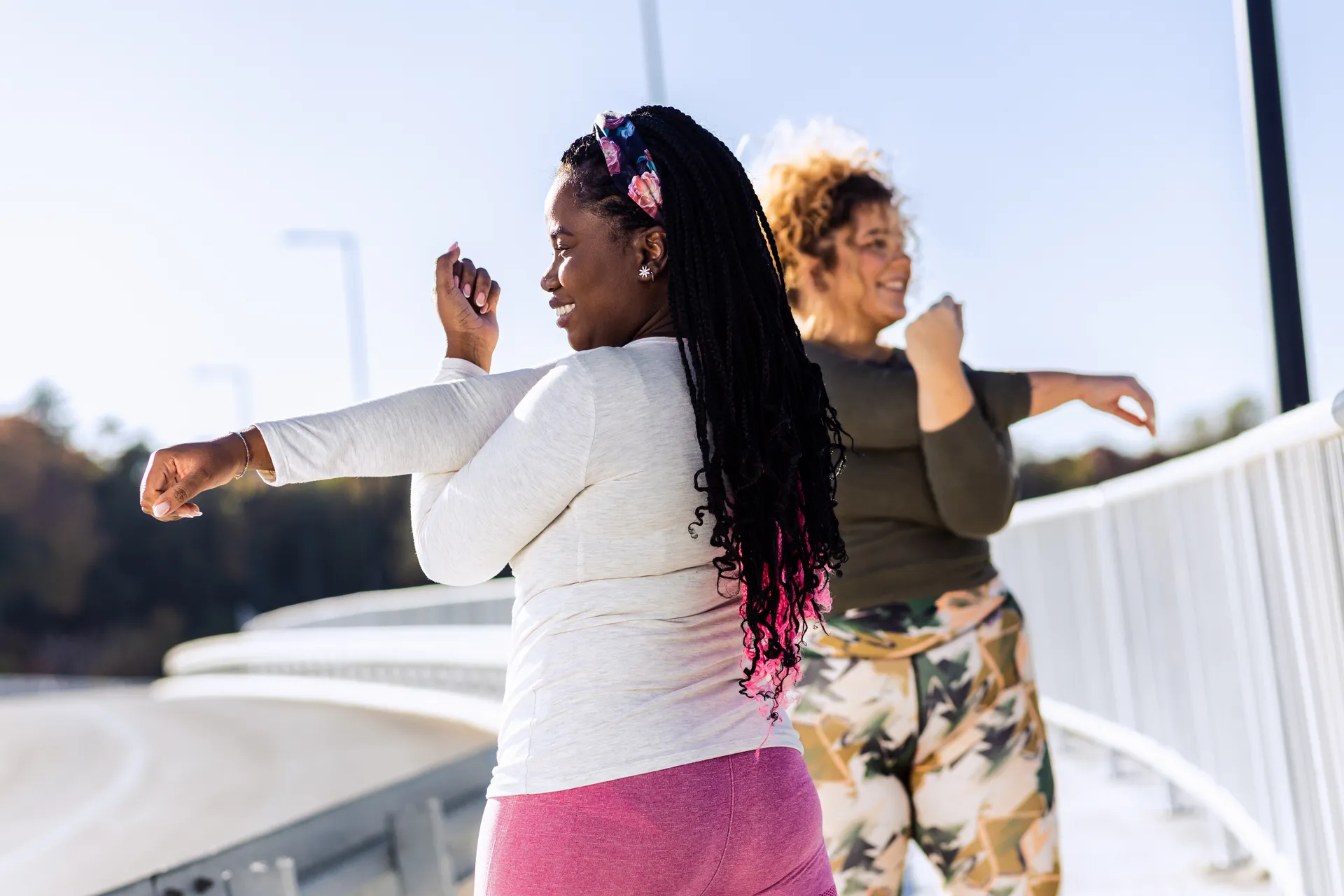 Two women smiling and stretching their arms outdoors on a sunny day.