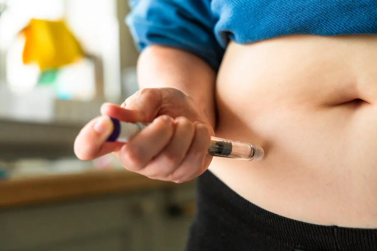 Person injecting insulin into their abdomen with a syringe pen.