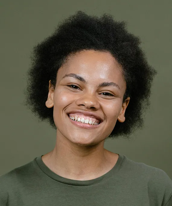 Smiling young woman with natural curly hair wearing a green shirt against a green background.