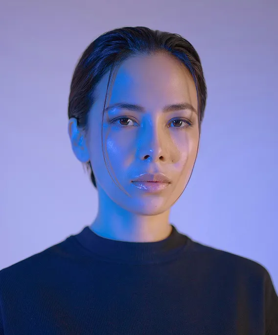 Portrait of a woman with wet hair and neutral expression under blue lighting on a plain background.