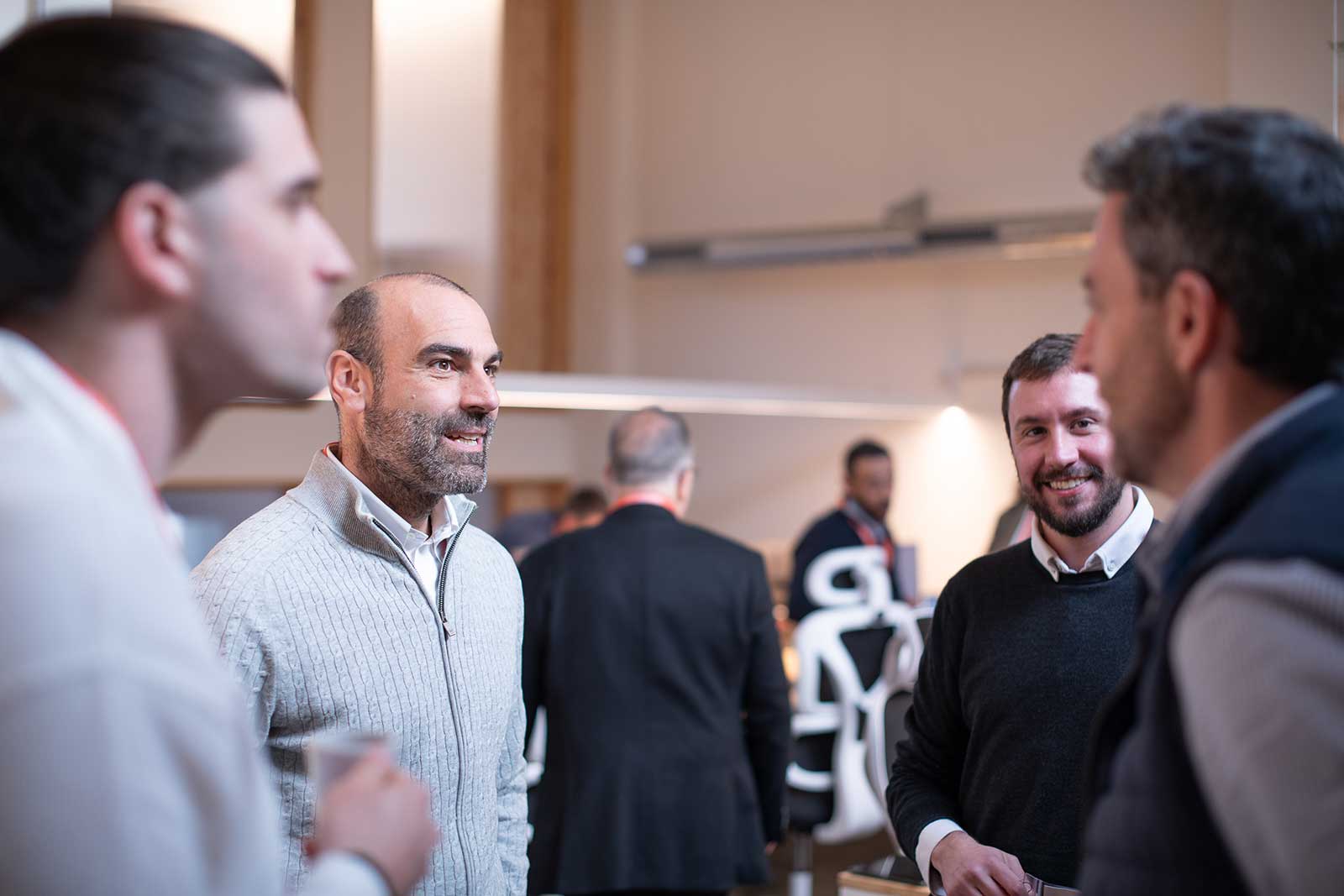 Grupo de hombres conversando y sonriendo en un entorno interior de oficina.