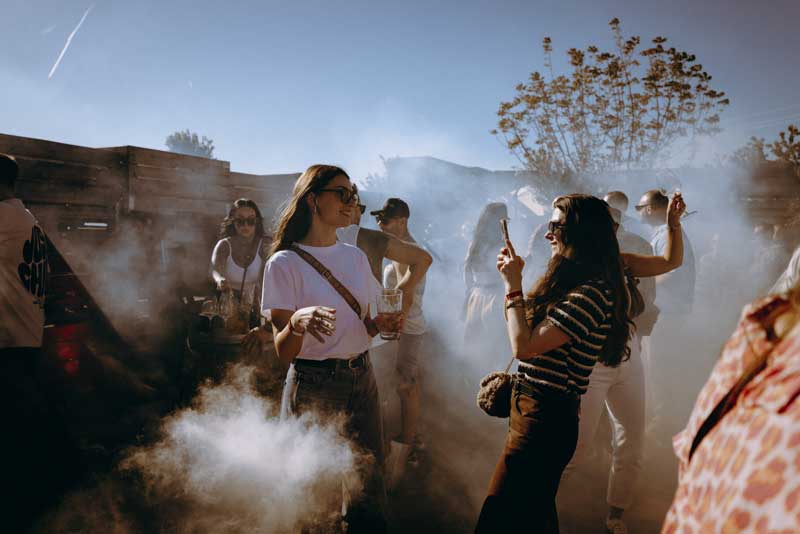 Junge Frauen genießen draußen bei Rauch und Sonne ein Festival oder Event.