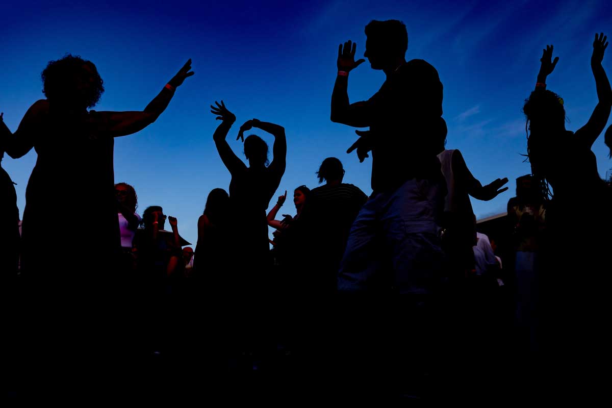 Menschen tanzen bei Sonnenuntergang mit dunklen Silhouetten vor blauem Himmel.