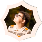 Boy wearing glasses looking up inside a white, irregular-shaped frame against a blurred dark background.