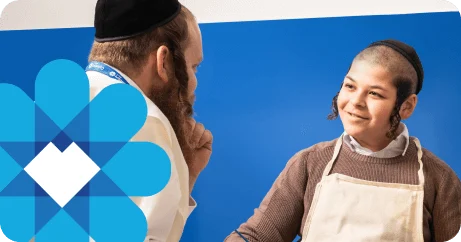 Man and boy wearing yarmulkes and aprons smiling at each other against a blue background.