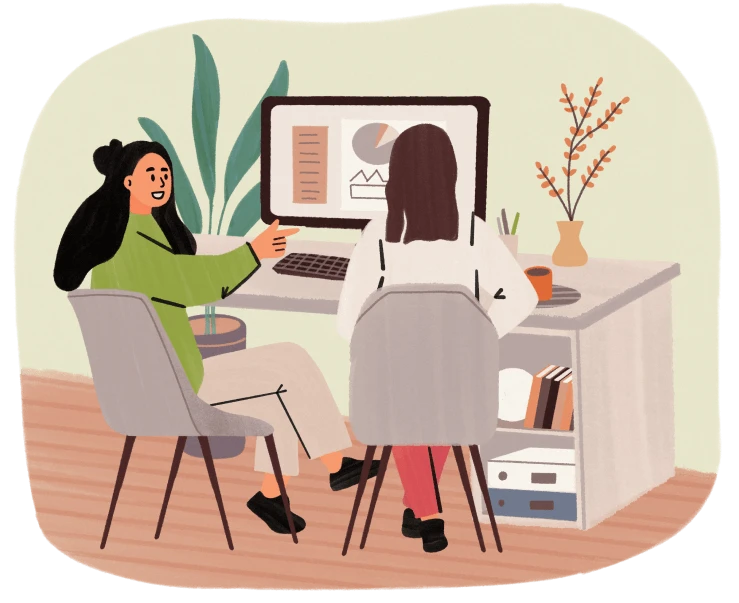 Two women sit at a desk discussing charts on a computer screen in a cozy office setting.