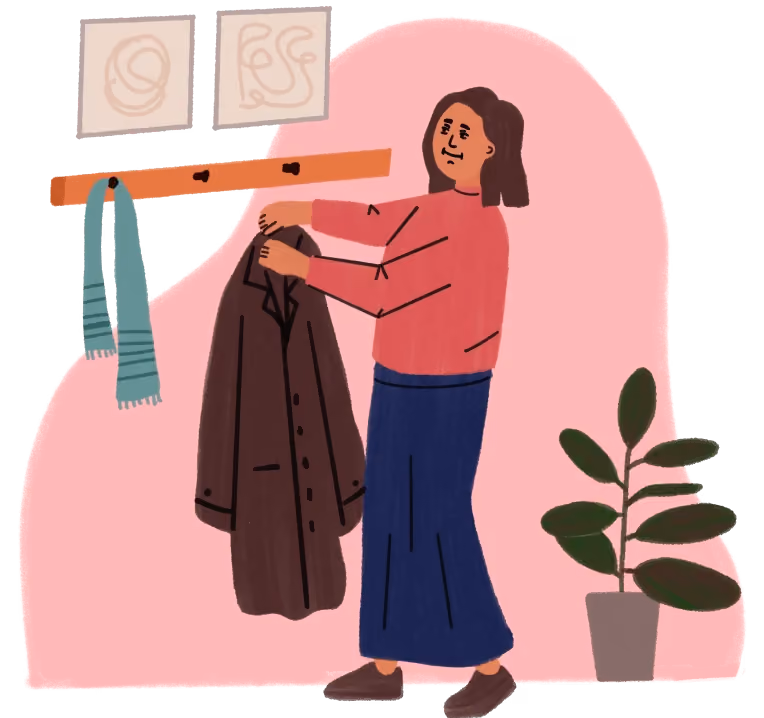 Person hanging a brown coat on a wall hook with a blue scarf and plant nearby.