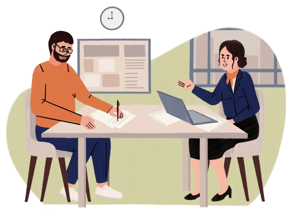 Man and woman sitting at a table in an office, talking and working with papers and a laptop.