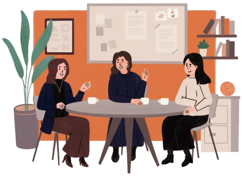 Three women sitting around a table having a conversation with coffee cups in a cozy room.