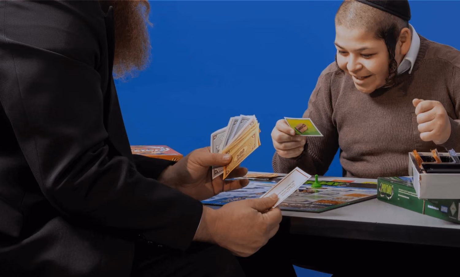 Two people playing a board game with money and cards, one person smiles excitedly.