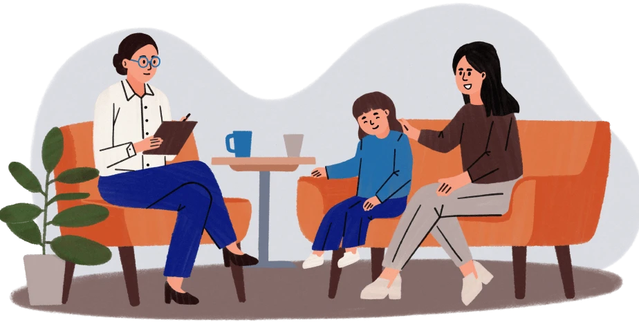 Woman therapist with clipboard talking to a mother and child seated on orange chairs.
