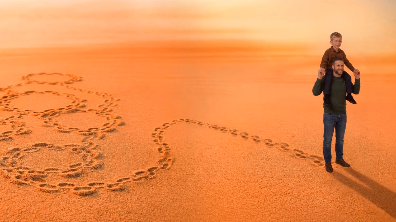 Man carrying a boy on shoulders walking on sand with footprints forming connected hearts.