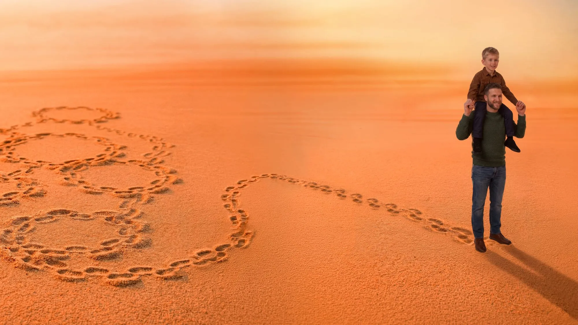 Man carrying a boy on shoulders walking on sand with footprints forming connected hearts.