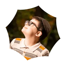 Boy wearing glasses and a hat looking up with a blurred green and yellow background.