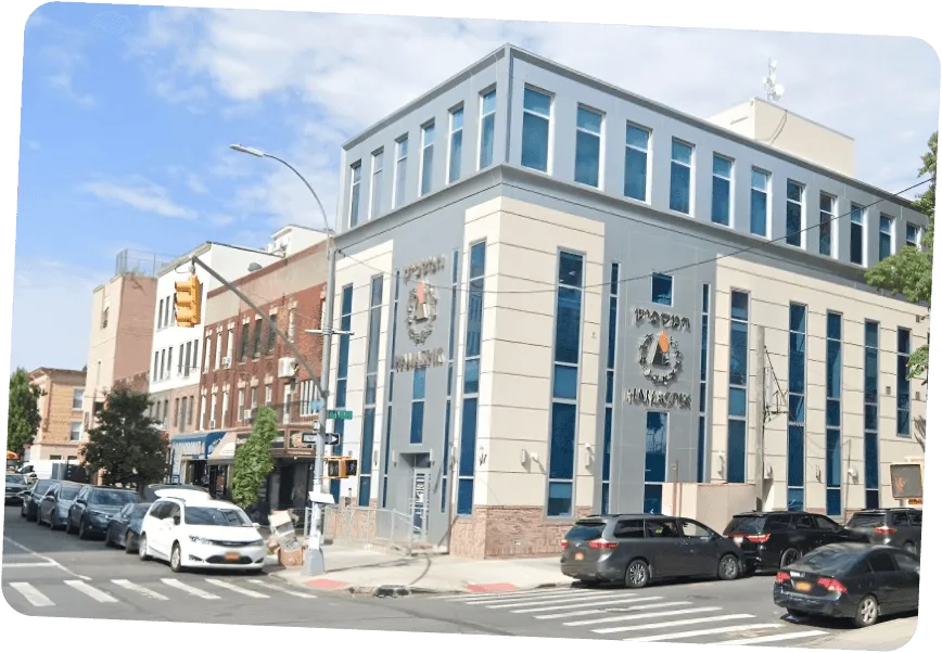 Corner view of a modern Boro Park building with multiple windows and parked cars on the street.