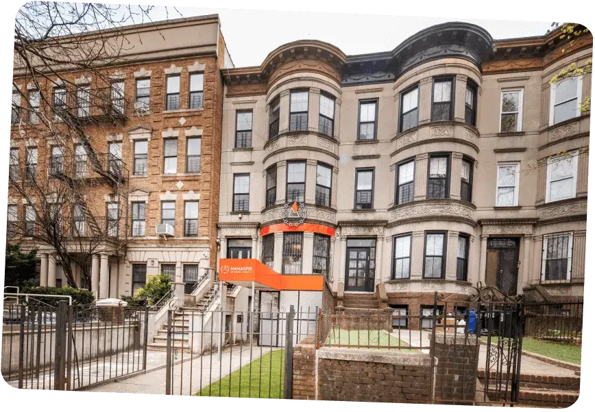 Row of brownstone townhouses with one building featuring an orange awning labeled Hamaspik.