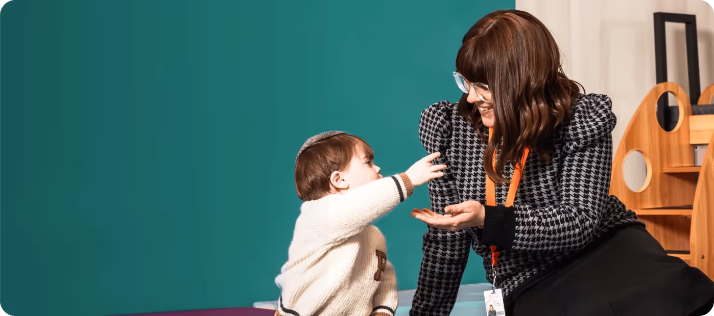 Young child reaching out to a smiling woman sitting and engaging with him