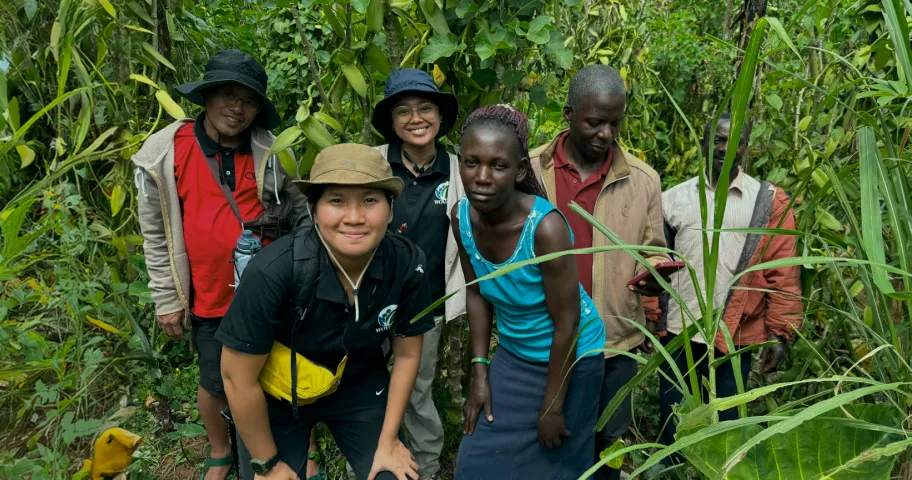 Five people standing on a green forest path, smiling and wearing casual outdoor clothing.
