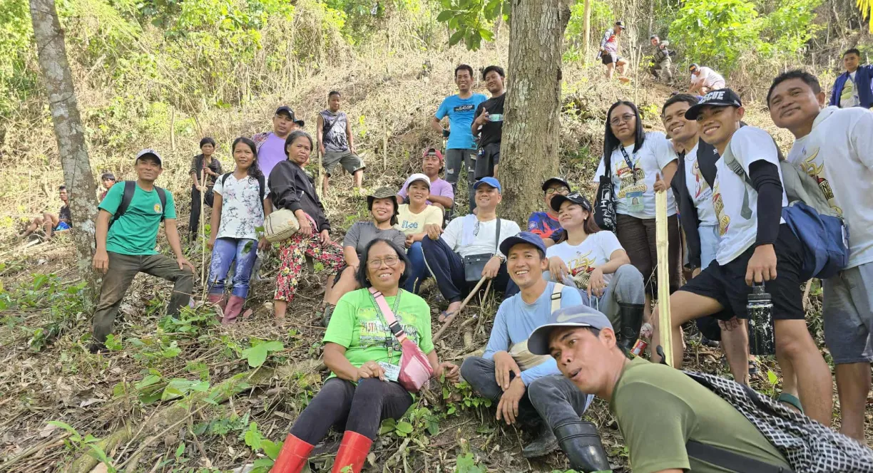 Group of people posing outdoors on a grassy hillside with trees in the background.