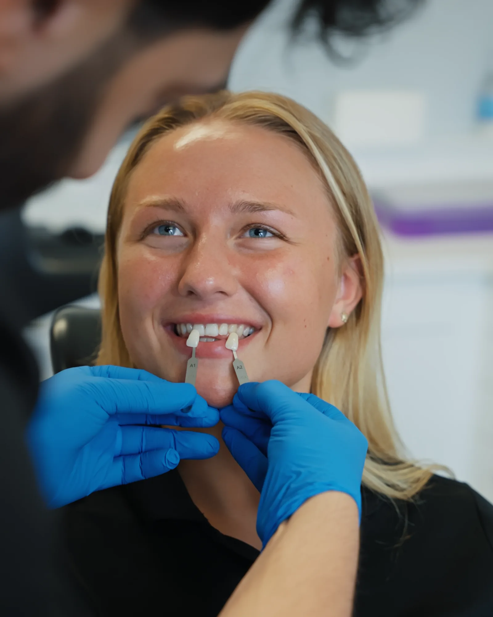 A smiling patient having her tooth shade checked against a shade guide at Sale Dental Spa