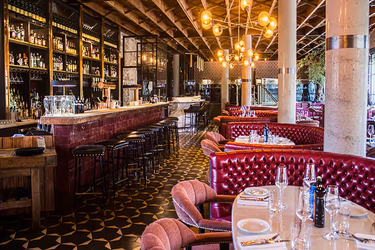 Long bar and burgundy tufted banquettes under globe chandeliers in an Eclective dining room