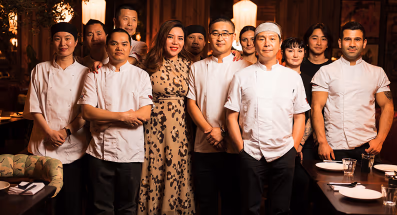 Chefs and floor team in whites gathered in a warmly lit dining room