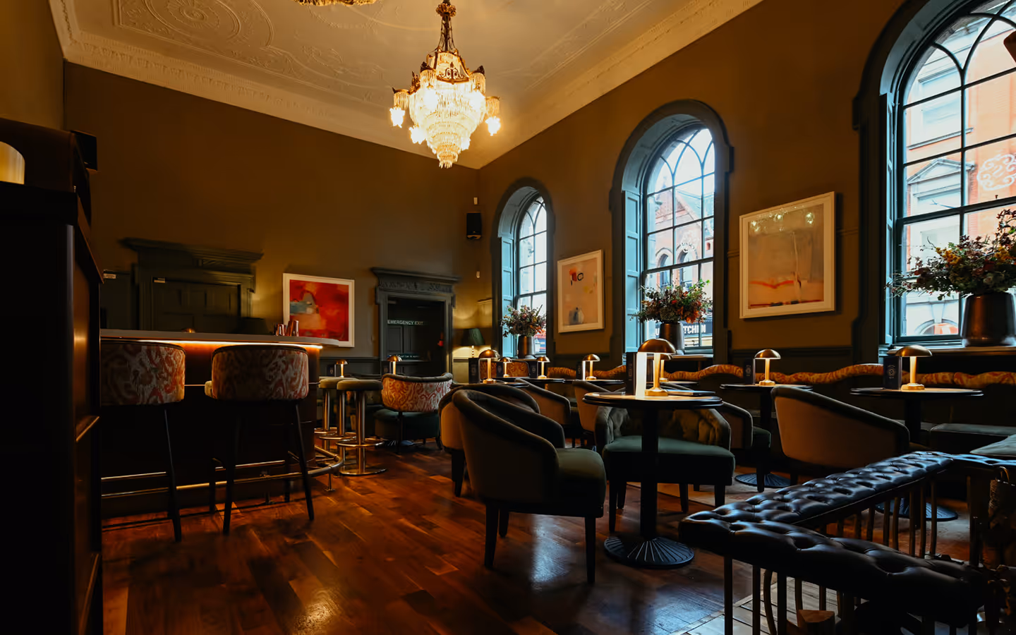 Chandelier above velvet armchairs and arched windows in the first-floor lounge at The Stapleton