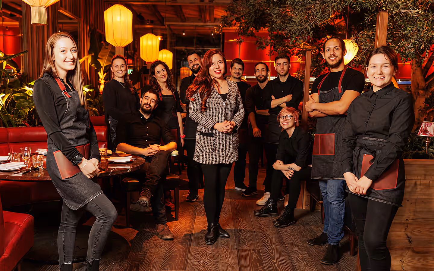 Front-of-house team in black aprons gathered in a lantern-lit dining room
